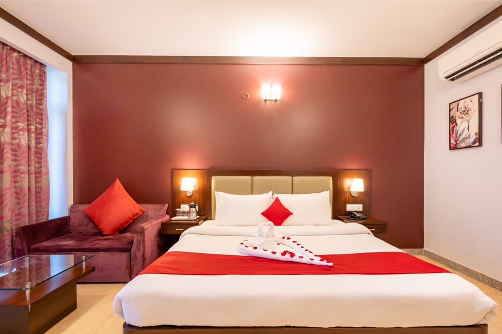 Deluxe room with red background of walls three beautifully lit lamps on the walls with a white sheet over bed kept aside a bright red sofa